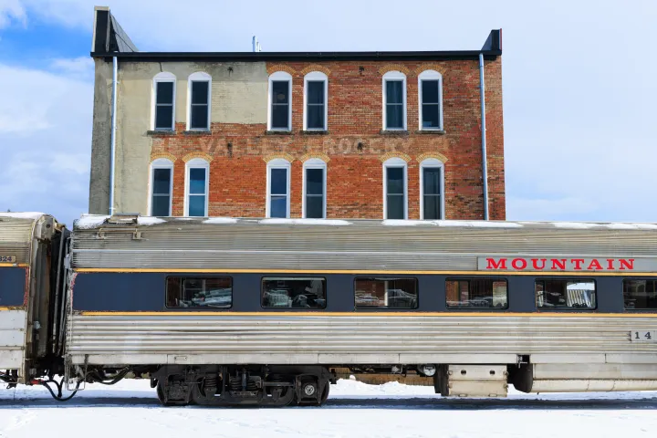 Vintage train car labeled 'MOUNTAIN' in front of brick building with snow on the ground.
