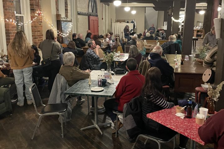 People seated at tables inside a cozy room with brick walls and hanging lights.
