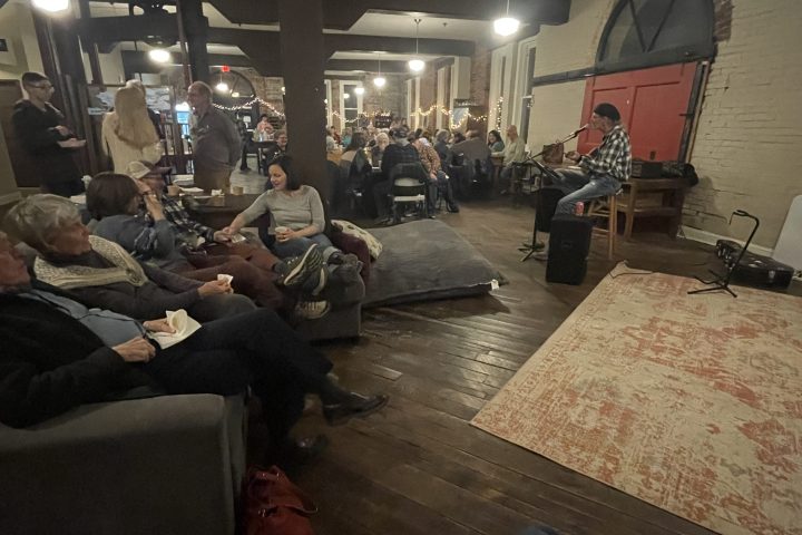 A cozy gathering with a musician playing guitar and people seated in a warmly lit room.