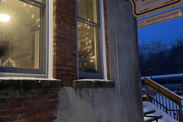 Sign for 'Golden Rule Marketplace' on a snowy sidewalk next to a brick building with lit windows.
