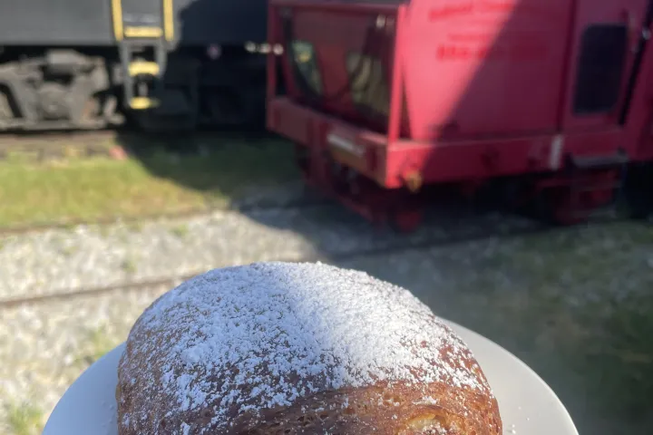Chocolate croissant on a plate held near red and black trains on tracks.