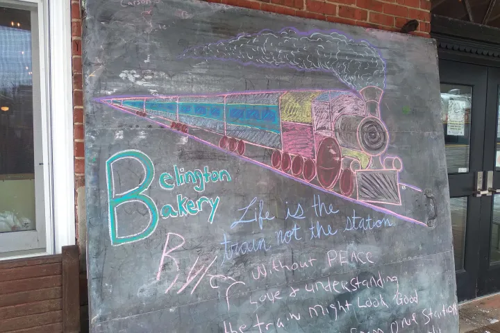 Chalk drawing of a train and text on a blackboard outside a brick building.