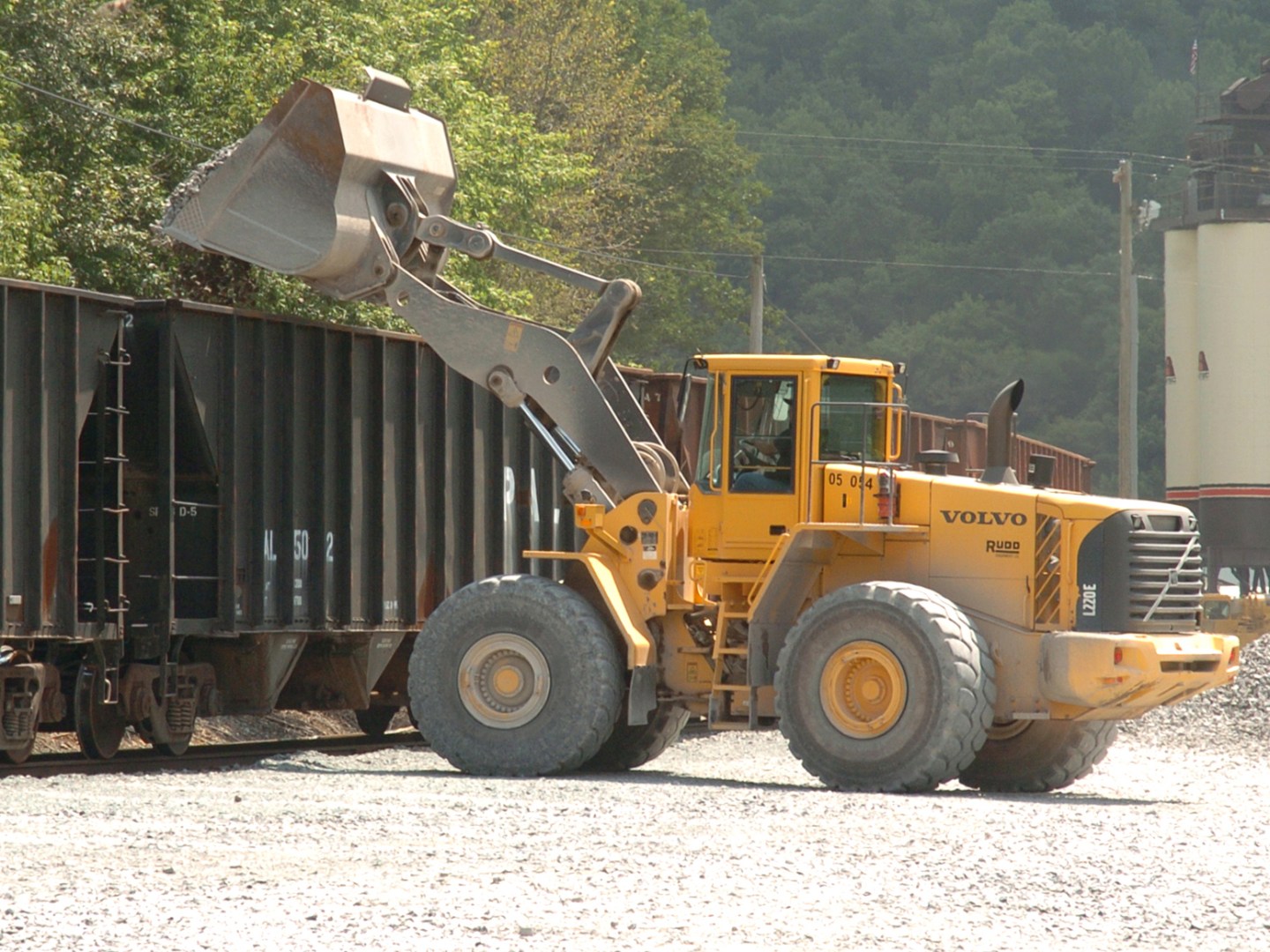 Yellow loader dumping gravel into a train car in a rural industrial area.