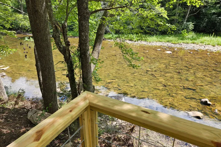 Wooden deck overlooking a rocky river with surrounding green trees.