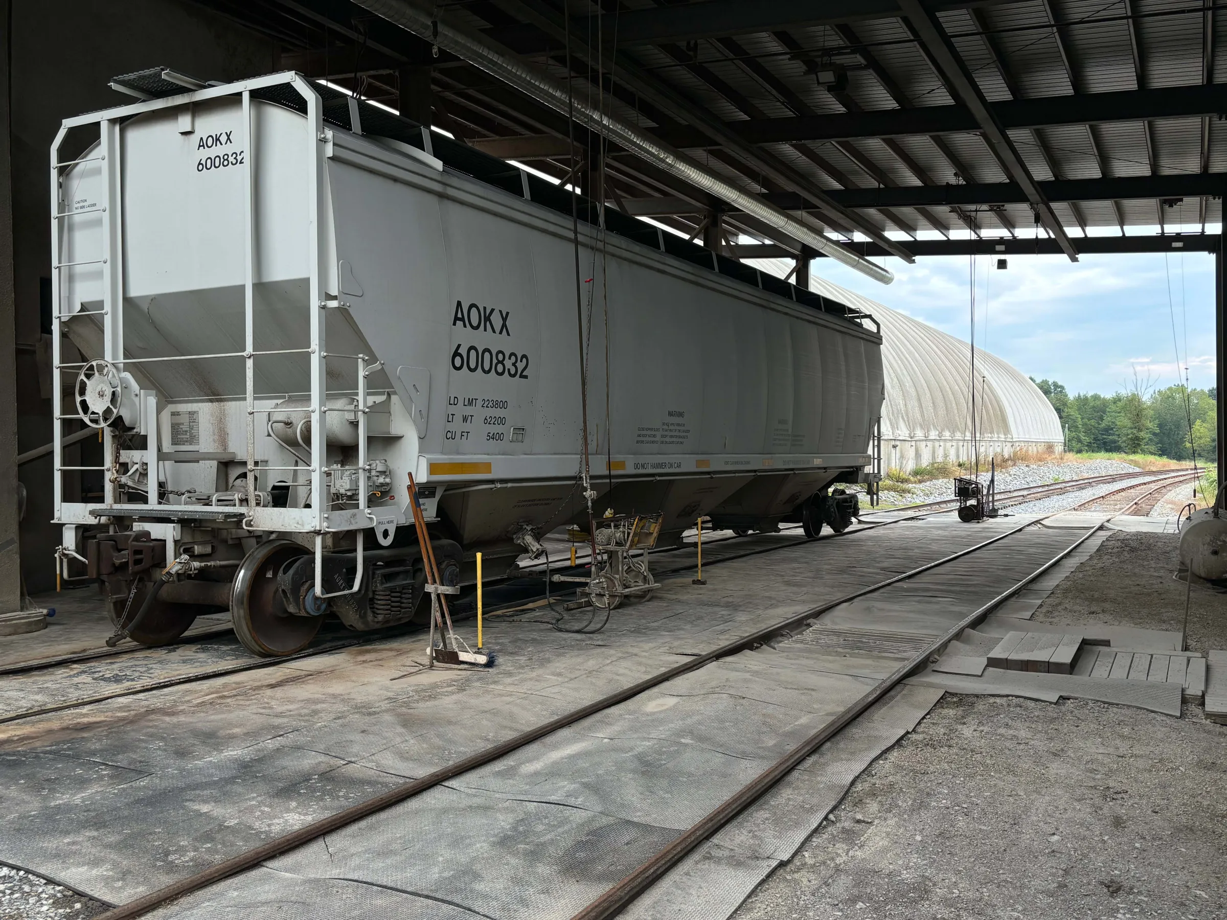 Freight train car under a metal roof by railway tracks, with clear sky visible in the background.