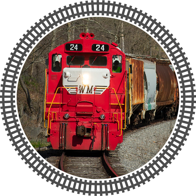 Red train with number 24 on front, moving on railroad surrounded by trees.