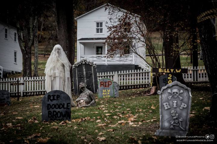 Halloween graveyard scene with ghost figure, tombstones, and a white house in the background.