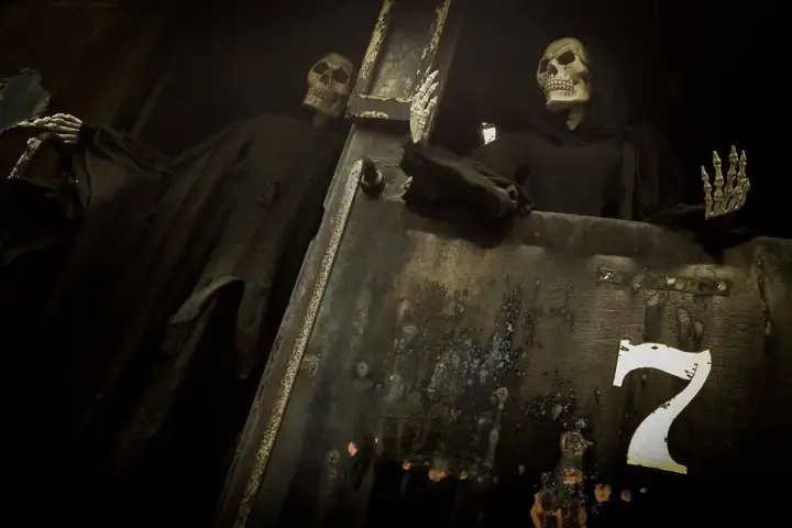 Skeleton figures in dark robes behind a worn door marked with the number seven.