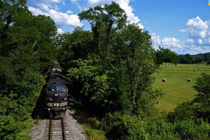 Train on tracks surrounded by lush greenery and fields with hay bales.